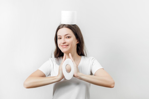 Een jonge vrouw in een wit t-shirt comprimeert in handen een rol wc-papier op een witte achtergrond