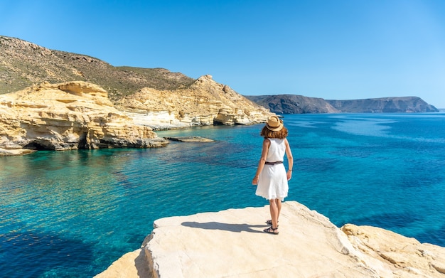 Een jonge vrouw in een witte jurk die op een mooie zomerdag naar de zee kijkt in Rodalquilar in Cabo de Gata, Almería