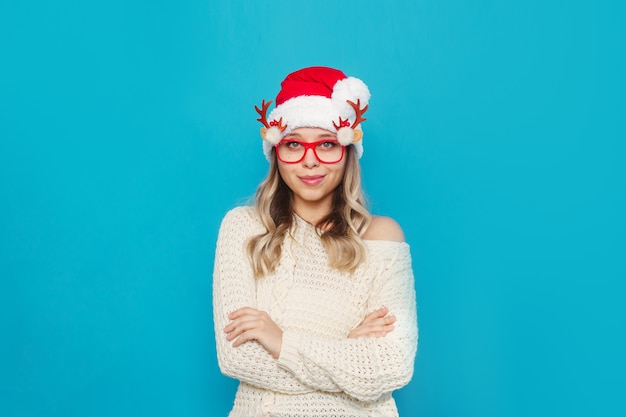 Een jonge vrouw in een witte trui Kerstmuts Kerstbril staat met haar armen over elkaar op haar buik