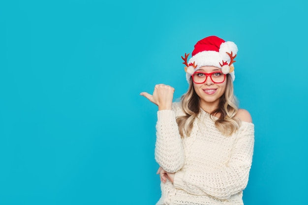 Een jonge vrouw in een witte trui Kerstmuts Kerstbril wijst naar lege kopieerruimte voor tekst