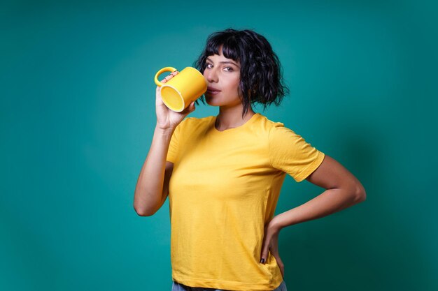 Een jonge vrouw in het geel drinkt uit een kopje melk. Studio opname, geïsoleerd op een gekleurde achtergrond.