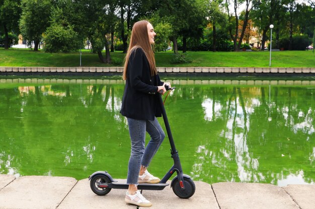 Een jonge vrouw in stijlvolle kleding poseert met een elektrische scooter op straat