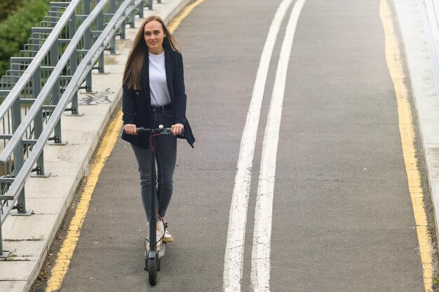 Een jonge vrouw in stijlvolle kleding rijdt op een elektrische scooter op een fietspad