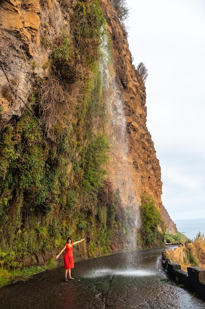 Een jonge vrouw kijkt naar de waterval die valt op de weg genaamd Anjos Waterfall Madeira