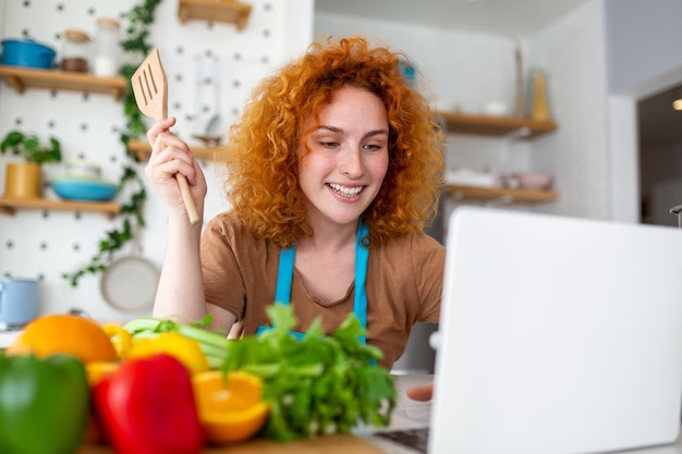 Een jonge vrouw leert koken, ze bekijkt videorecepten op een laptop in de keuken en kookt een gerecht Koken thuis concept