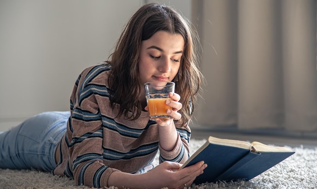 Een jonge vrouw leest een boek en drinkt sinaasappelsap