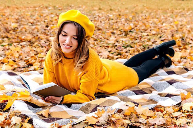 Een jonge vrouw leest een boek in een herfstpark op een deken Een meisje in een gele trui en baret