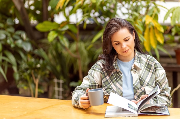 Een jonge vrouw leest een boek over het kweken en verzorgen van planten terwijl ze aan een tafel zit in een prachtige omgeving met veel planten Banner met plaats voor tekst