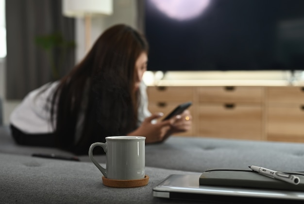 Een jonge vrouw ligt op de bank tijdens het gebruik van de mobiele telefoon in de woonkamer