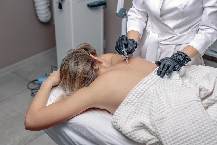 Een jonge vrouw ligt op een bank op haar buik en krijgt injecties in de rug om gewrichtspijn te verlichten
