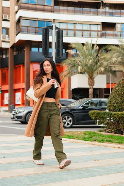 Een jonge vrouw loopt op straat met vrijetijdskleding en een thermoskan