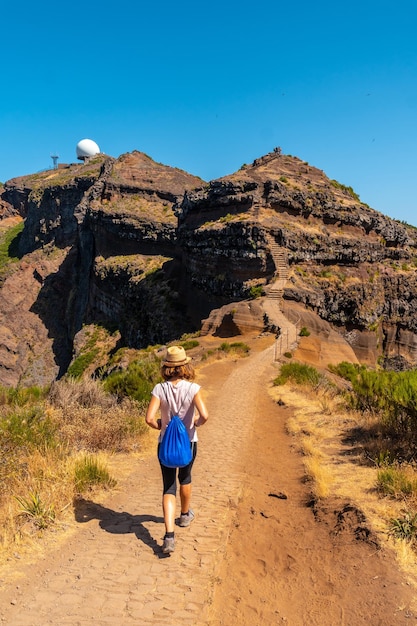 Een jonge vrouw loopt richting pico do arieiro vanuit het uitkijkpunt ninho da manta, madeira portugal