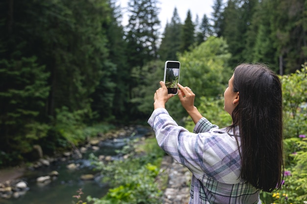 Een jonge vrouw maakt een foto in de bergen in het bos op een smartphone