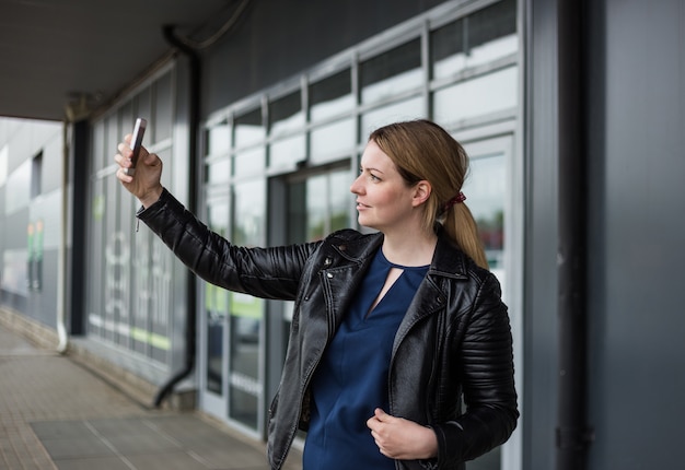 Een jonge vrouw maakt een foto van zichzelf op haar telefoon bij een winkelcentrum