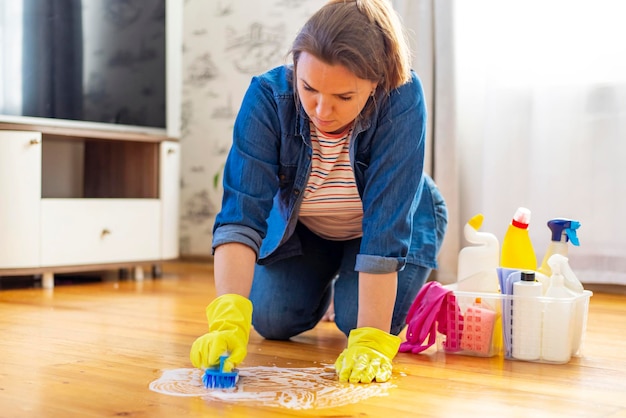 Een jonge vrouw met beschermende handschoenen wast de vloer met een borstel en wasmiddel