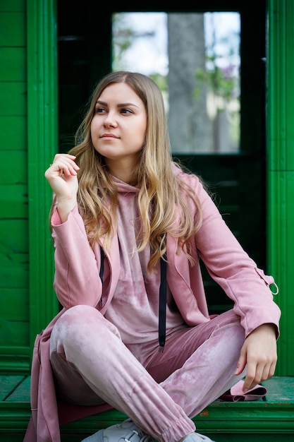 Een jonge vrouw met blond haar van Europees uiterlijk zit op de trap. Meisje in een roze pak en sneakers