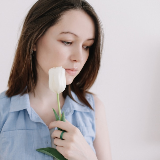 een jonge vrouw met donker steil haar met tulpen tegen een lichte muur