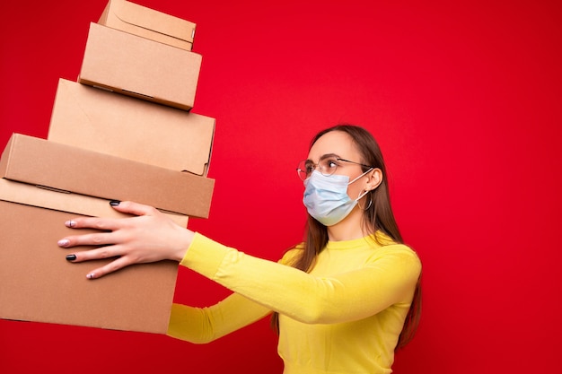 Een jonge vrouw met een beschermend masker houdt kartonnen dozen vast om te verplaatsen op een rode achtergrond