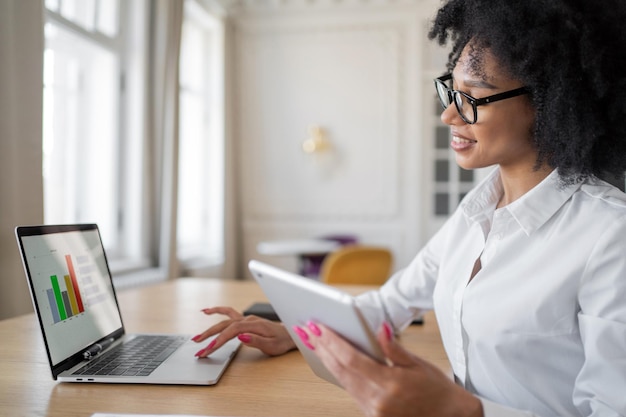 Een jonge vrouw met een bril en een wit overhemd op kantoor typt een bericht met een laptop