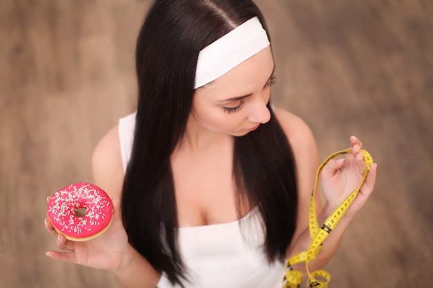 Een jonge vrouw met een donut en een meetlint. Een meisje staat op een houten. Het uitzicht vanaf de top. Van gezond eten. Dieet.