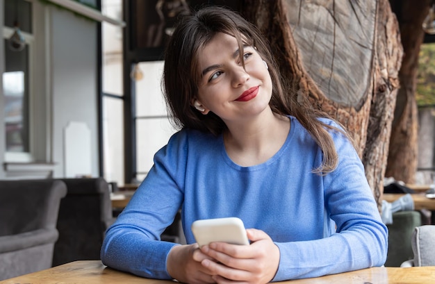 Een jonge vrouw met een draadloze koptelefoon gebruikt de telefoon terwijl ze in een café zit