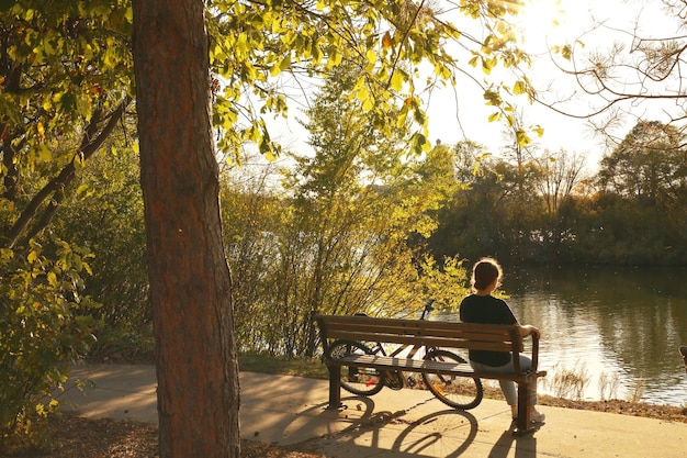 Een jonge vrouw met een fiets zit op een bankje bij het meer Herfstfoto in het park bij het meer