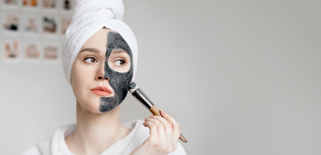 Een jonge vrouw met een handdoek op haar hoofd brengt een natuurlijk zwart cosmetisch masker met actieve kool aan