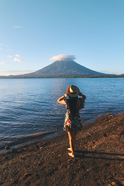 Een jonge vrouw met een hoed die aan de oever van het meer staat met een prachtig uitzicht op de Concepcion-vulkaan op het eiland Ometepe, Nicaragua