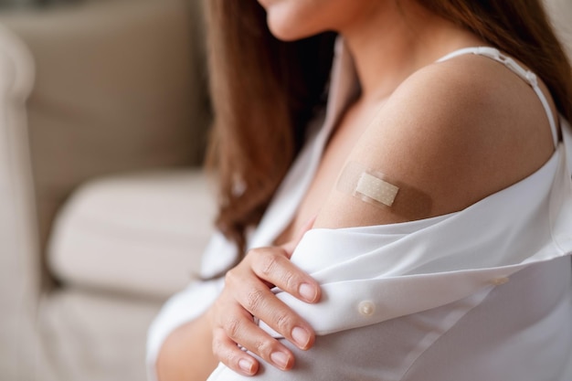 Een jonge vrouw met een kleverige verband medische gips bandhulp op haar schouder voor vaccinatie concept