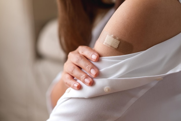 Een jonge vrouw met een kleverige verband medische gips bandhulp op haar schouder voor vaccinatie concept