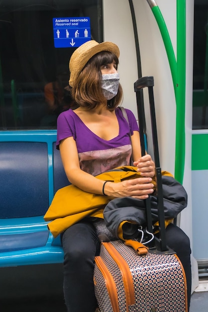 Een jonge vrouw met een koffer en een hoed zit te wachten op de metro