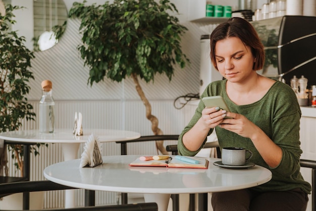 Een jonge vrouw met een kort kapsel zit aan een tafel in een café