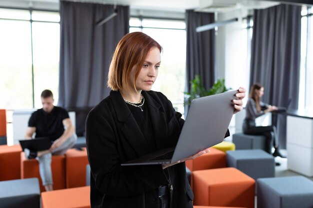 Een jonge vrouw met een laptop op de achtergrond van een werkend kantoor