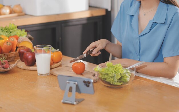 Een jonge vrouw met een mooi gezicht in een blauw shirt met lang haar die fruit eet en thuis in de keuken zit met een laptop en een notitieboekje voor ontspanning Concept vakantie