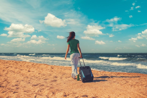 Een jonge vrouw met een reistas die op het strand loopt