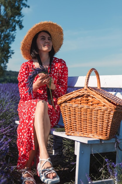 Een jonge vrouw met een strohoed zit op een bankje in een lavendelveld en weeft een krans