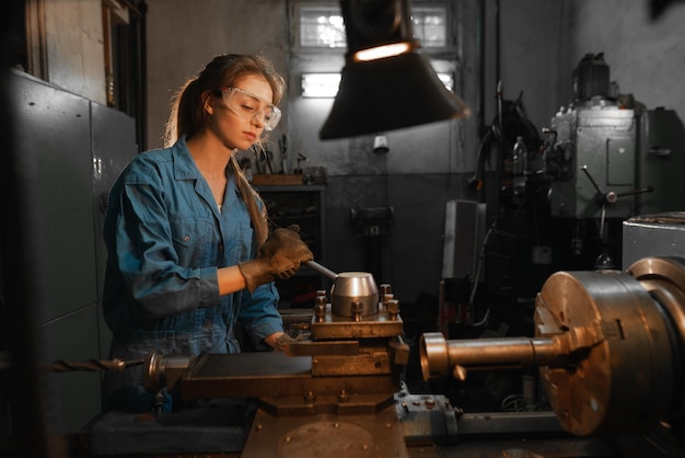 Een jonge vrouw met een veiligheidsbril en overall staat bij de draaibank Beroepsconcept Turner Metalworking Turning Industry Metal