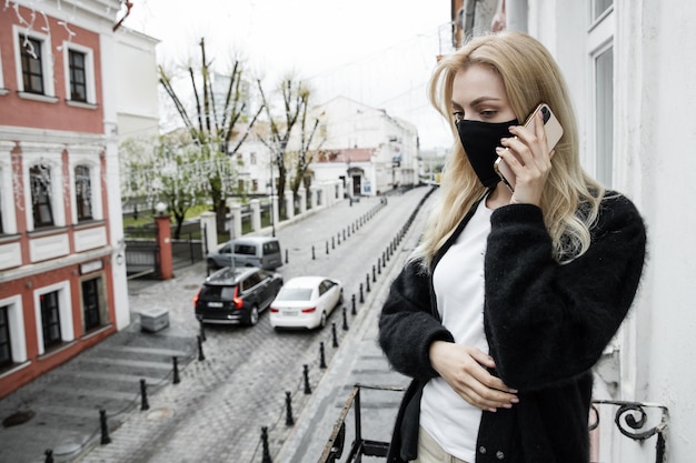 Een jonge vrouw met een zwart masker staat op het balkon van het kantoor te telefoneren