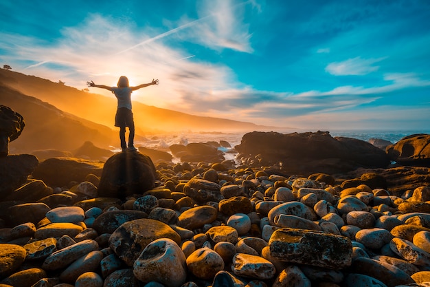 Een jonge vrouw met haar armen wijd open bij zonsondergang aan de kust van Jaizkibel bij San Sebastian. Baskenland