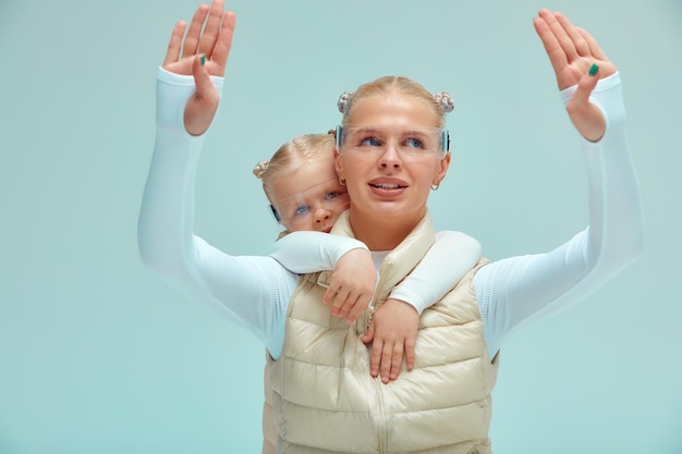 Foto een jonge vrouw met haar dochtertje in witte hightech-kleding die een slimme bril draagt en met de handen tegen een holografisch scherm drukt