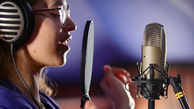 Een jonge vrouw met koptelefoon die door het popfilter in de studio zingt