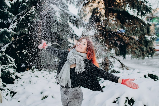 Een jonge vrouw met rood haar gooit sneeuw in de lucht op een zonnige winterdag wintervakantie