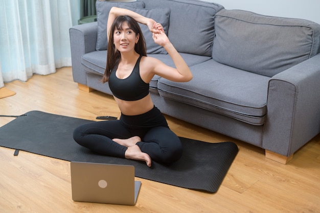 Een jonge vrouw oefent en kijkt naar online fitnesstraining op de laptop in de woonkamer thuis, sport, fitness en technologieconcept.