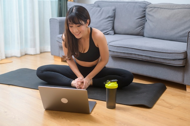 Een jonge vrouw oefent en kijkt naar online fitnesstraining op de laptop in de woonkamer thuis, sport, fitness en technologieconcept.