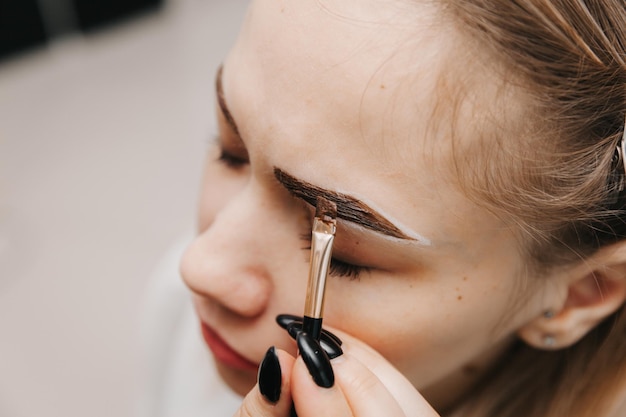 Een jonge vrouw ondergaat een wenkbrauwcorrectieprocedure in een schoonheidssalon close-up het meisje schildert haar wenkbrauwen in de salon