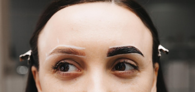 Foto een jonge vrouw ondergaat een wenkbrauwcorrectieprocedure in een schoonheidssalon close-up het meisje schildert haar wenkbrauwen in de salon