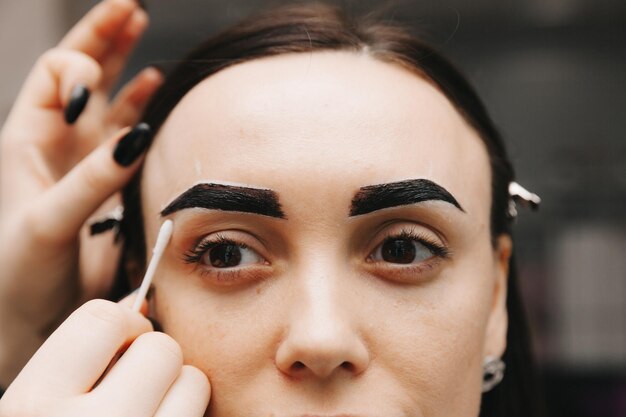 Een jonge vrouw ondergaat een wenkbrauwcorrectieprocedure in een schoonheidssalon close-up het meisje schildert haar wenkbrauwen in de salon