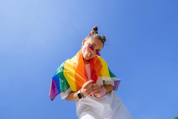 Een jonge vrouw ontwikkelt een regenboogvlag tegen de lucht