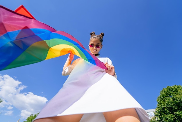 Een jonge vrouw ontwikkelt een regenboogvlag tegen de lucht