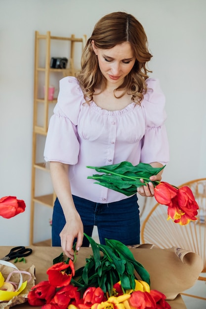 Een jonge vrouw pakt een feestelijk boeket in inpakpapier De bloemist maakt een assemblage met rode tulpen in de werkplaats Een vrouw aan het werk in een klein bedrijf of hobby